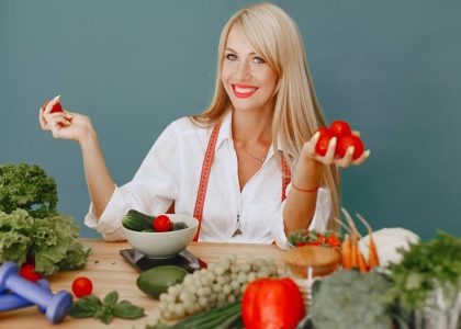 Healthy lifestyle concept with woman holding tomatoes and surrounded by fresh vegetables in a studio setting.