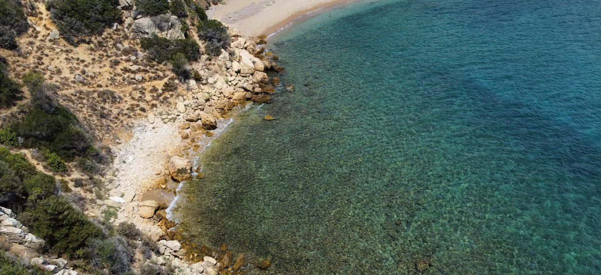 Aerial shot of a serene beach cove with clear turquoise waters and rocky shoreline.